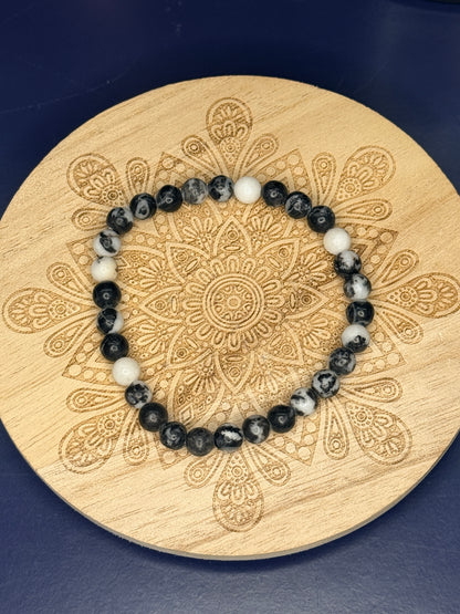 Black and white beaded zebra jasper bracelet resting on a decorative wooden coaster on a blue background