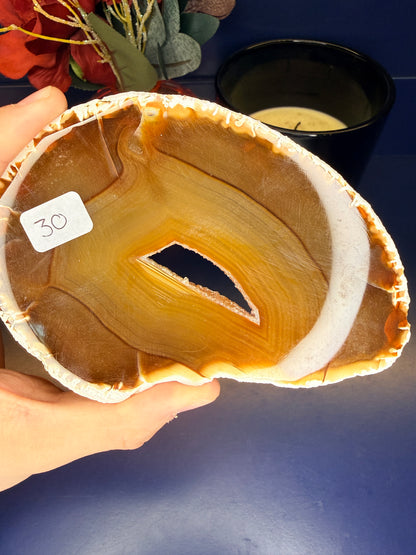 Hand holding an amber colored agate slice with a druzy in the middle in front of a red flower and black candle jar