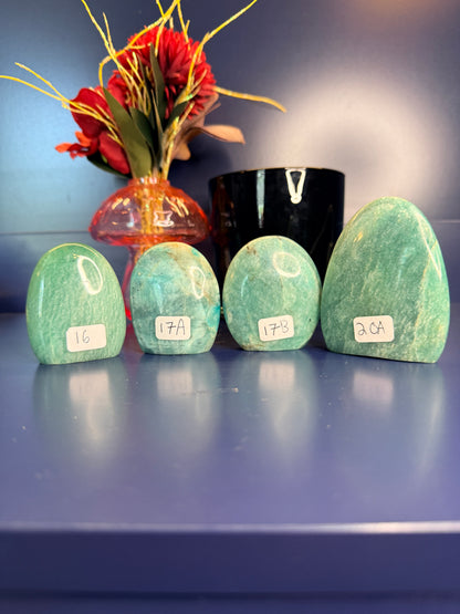Four blue green oblong amazonite free forms in front of a red flower in a vase and a black jar on a blue background