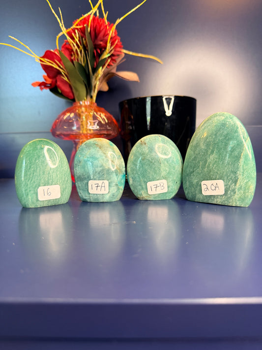 Four blue green oblong amazonite free forms in front of a red flower in a vase and a black jar on a blue background
