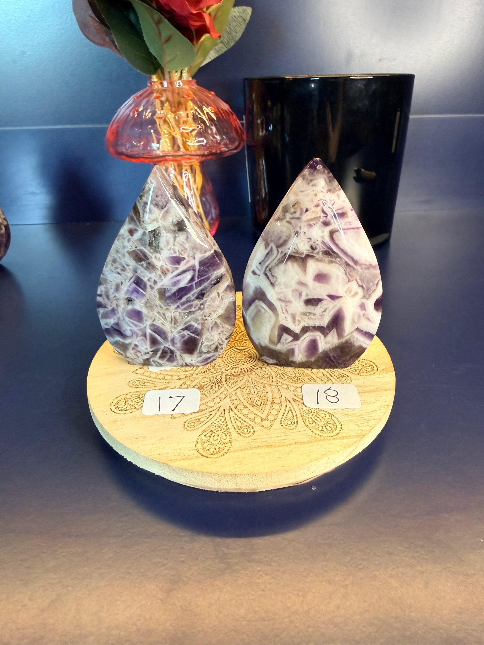 Two amethyst crystal freeforms on a wooden coaster with numbers 17 and 18, in front of a vase and jar