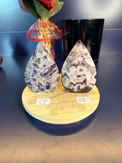 Two amethyst crystal freeforms on a wooden coaster with numbers 17 and 18, in front of a vase and jar