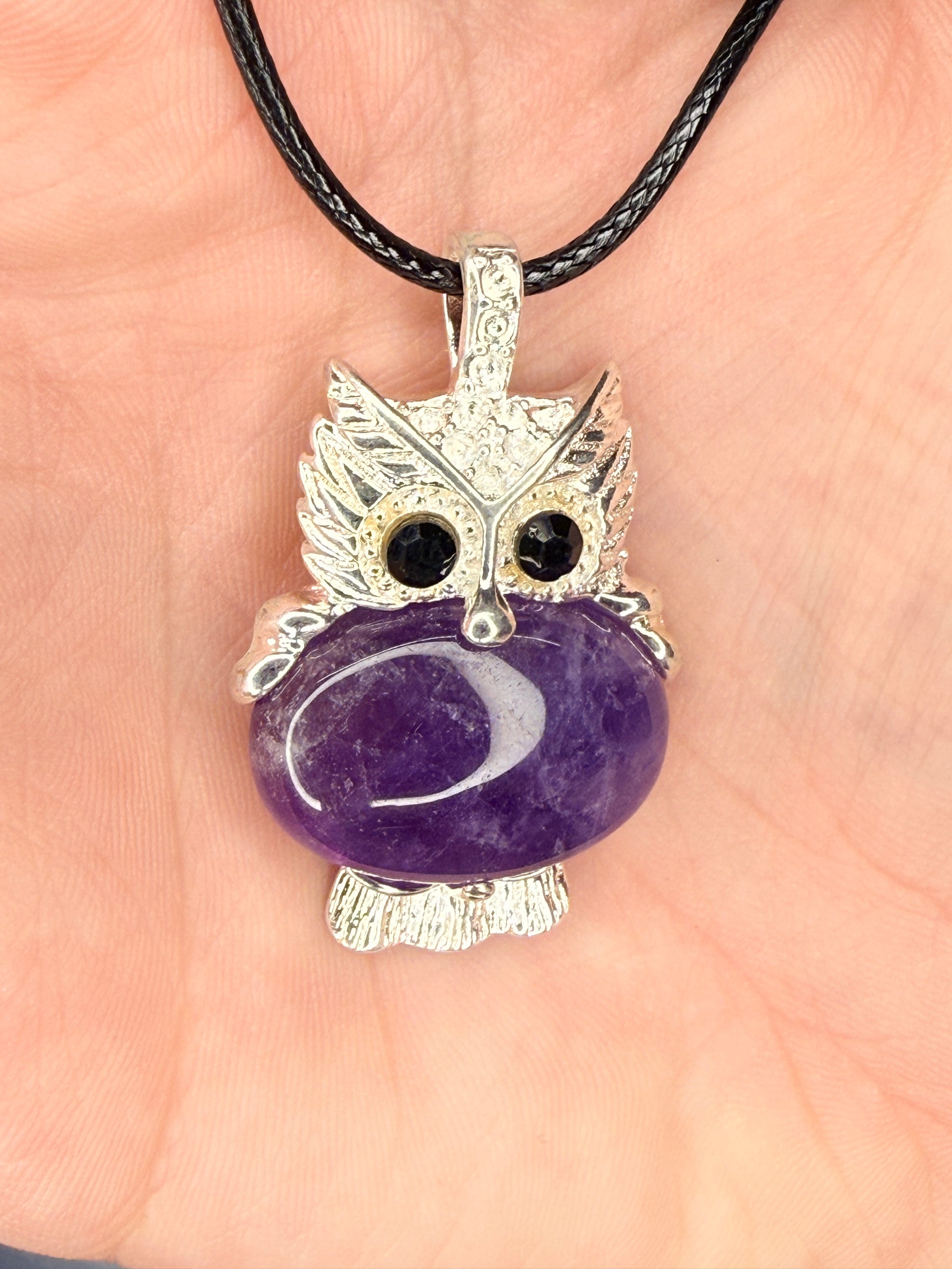 Hand holding an amethyst owl pendant attached to a nylon chain
