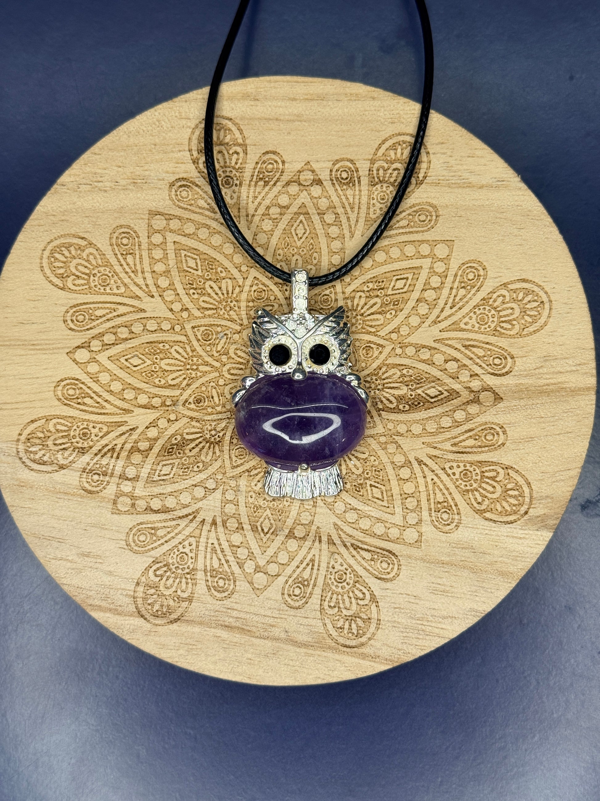 Amethyst owl pendant sitting on a decorative wooden coaster on a blue background
