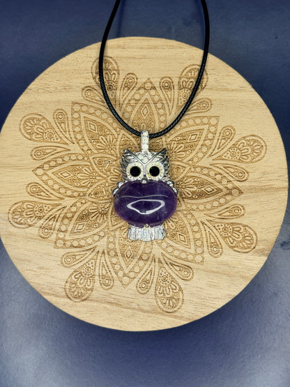 Amethyst owl pendant sitting on a decorative wooden coaster on a blue background
