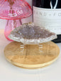 Pale purple Amethyst raw specimen on a wooden coaster in front of a black candle jar and pink vase