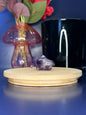 Purple amethyst shark carving in front of a pink vase and black jar on a wooden coaster against a blue background