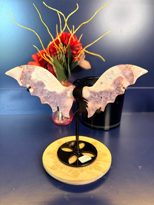 Pair of pink and purple crystal dragon wings on a wooden coaster in front of red flowers and a black jar