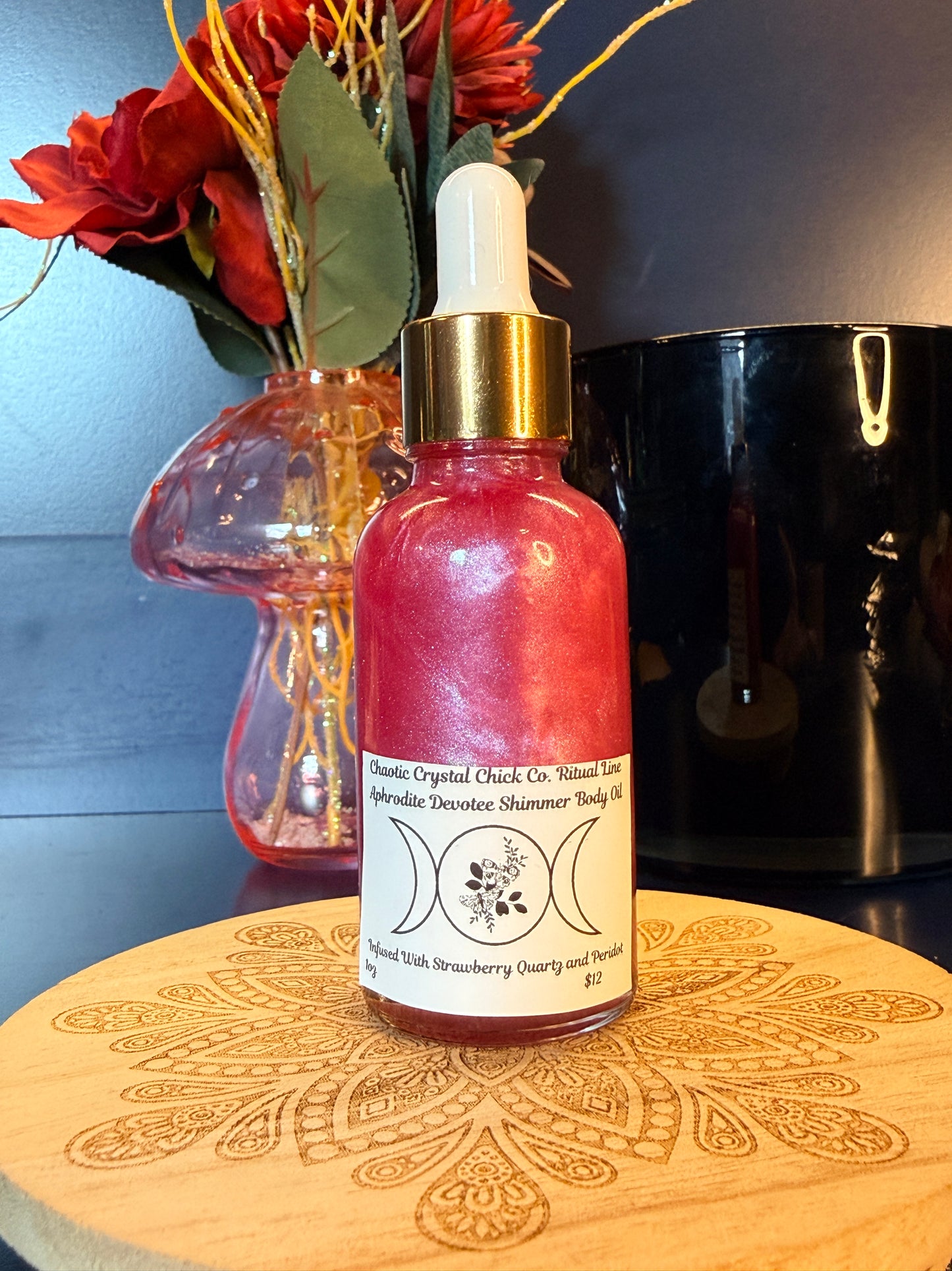 Pink bottle with gold cap on a decorative wooden coaster next to flowers