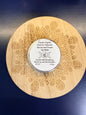 Wooden coaster with intricate patterns and a round metal lip balm on a dark blue background
