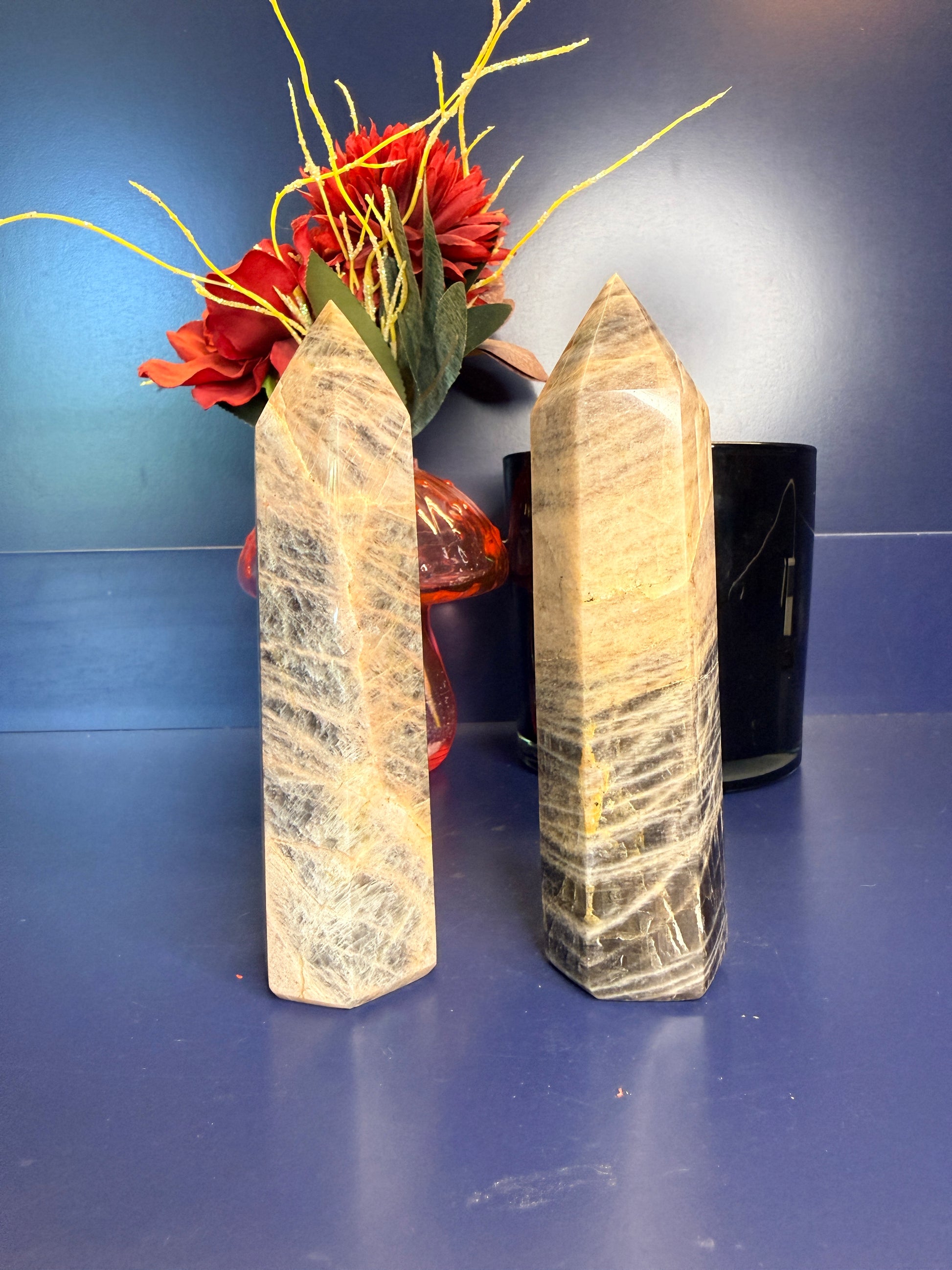 Two large black moonstone towers in front of a red flower and black jar on a blue background