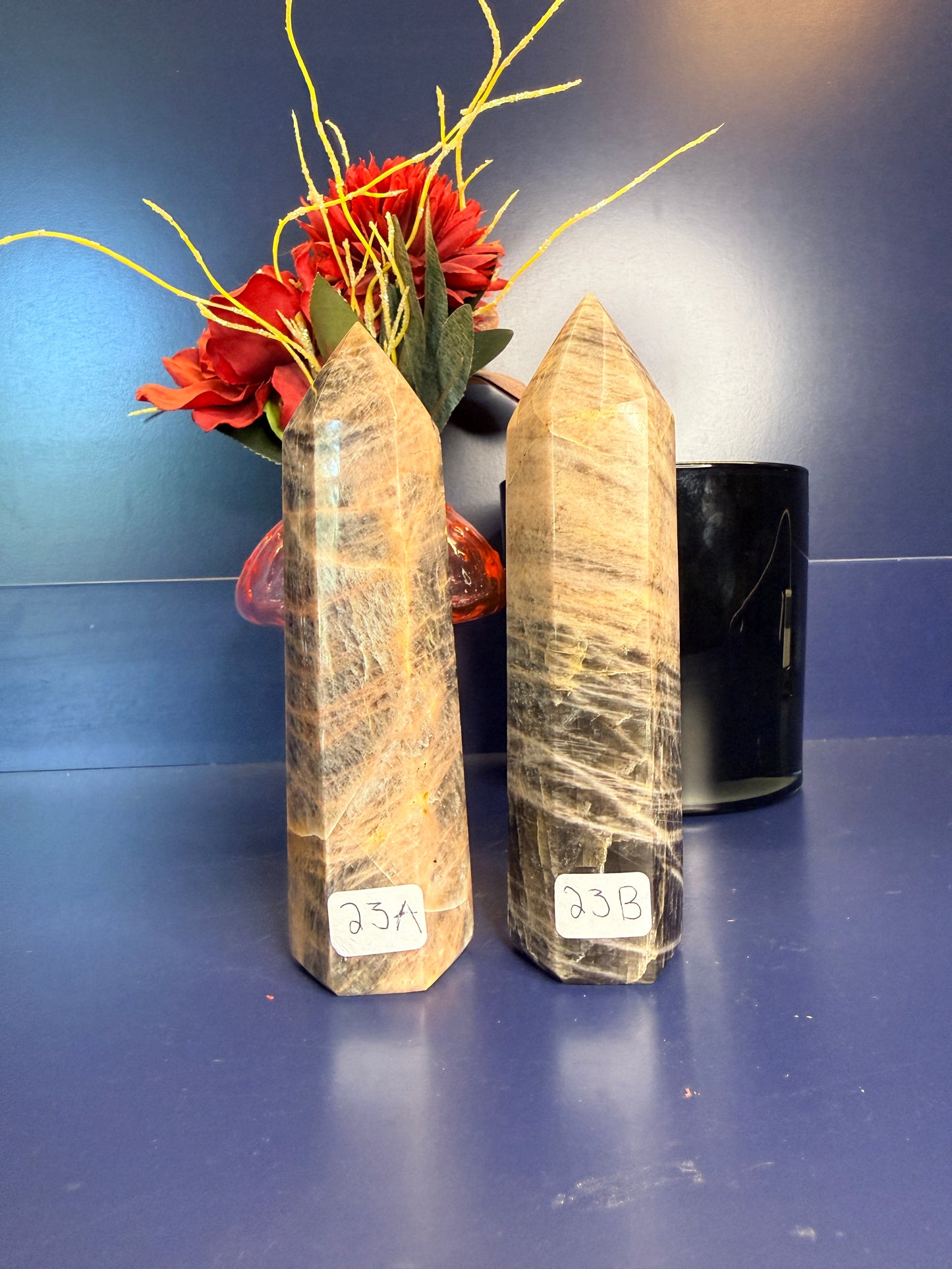 Two large black moonstone towers in front of a red flower and black jar on a blue background