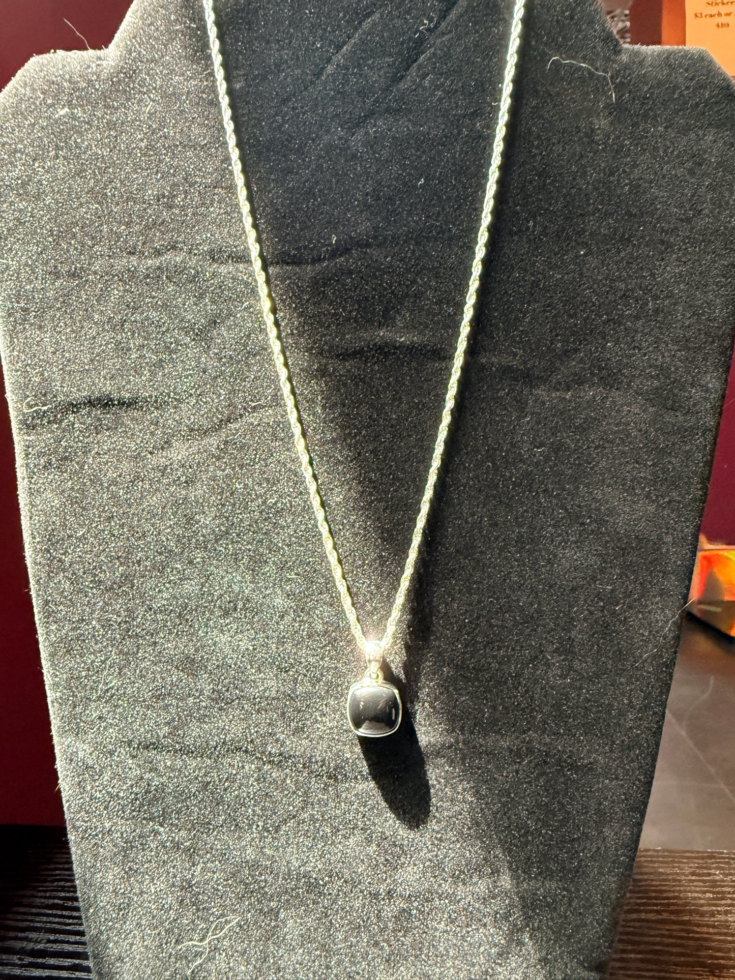 Sterling silver chain resting on a black velvet jewelry stand holding a square black onyx pendant