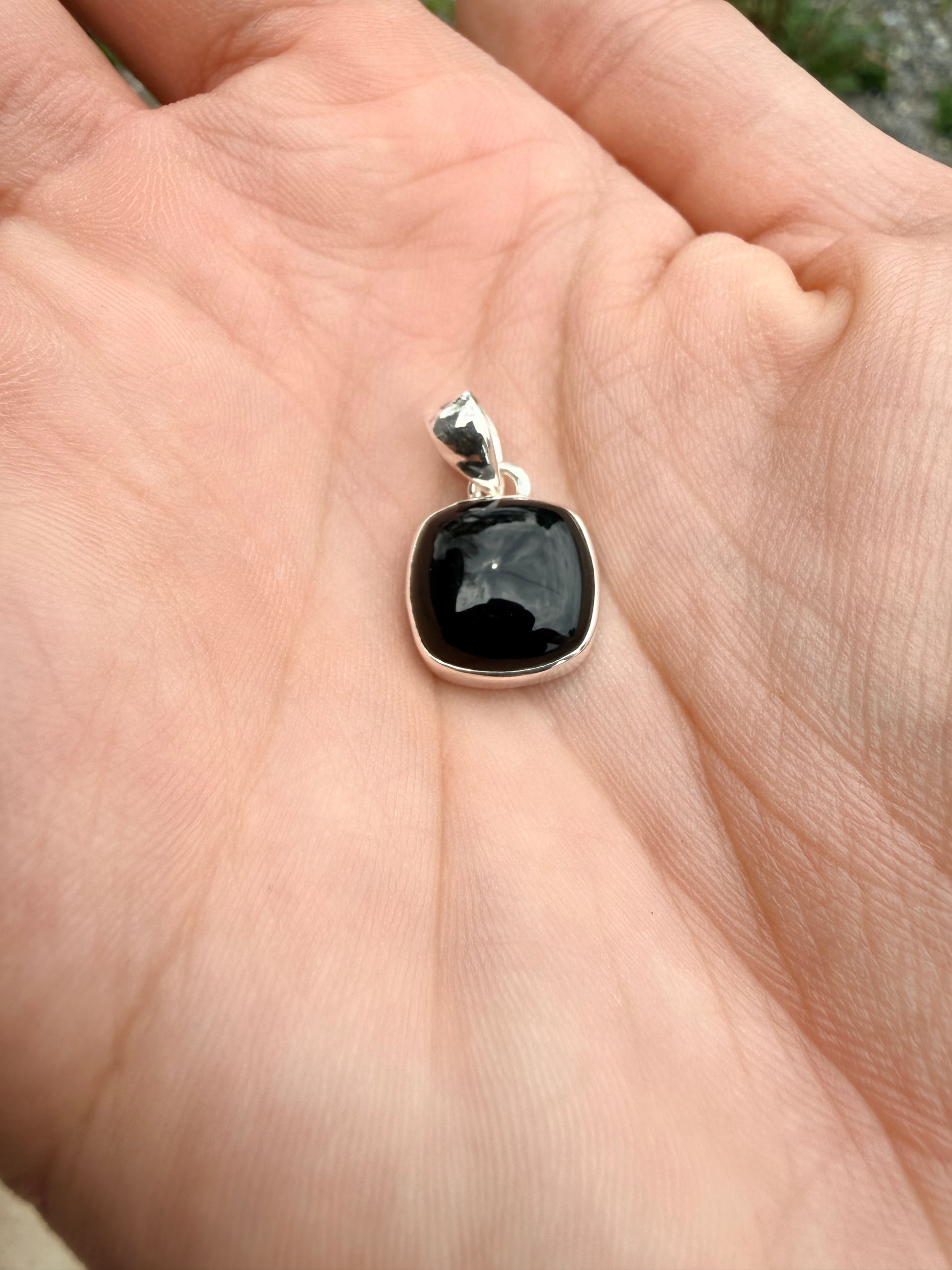 Hand holding a square black onyx sterling silver pendant