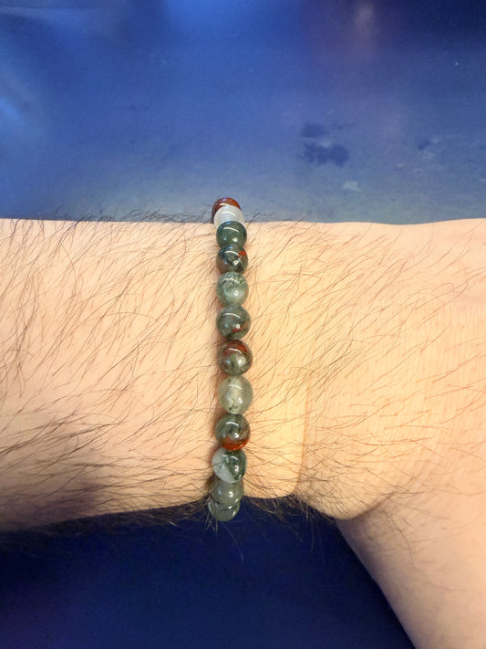 Red and green beaded bracelet on a wrist with a blue background