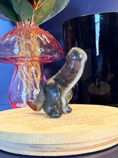 Multicolored bloodstone crystal sitting in front of a mushroom vase and black jar