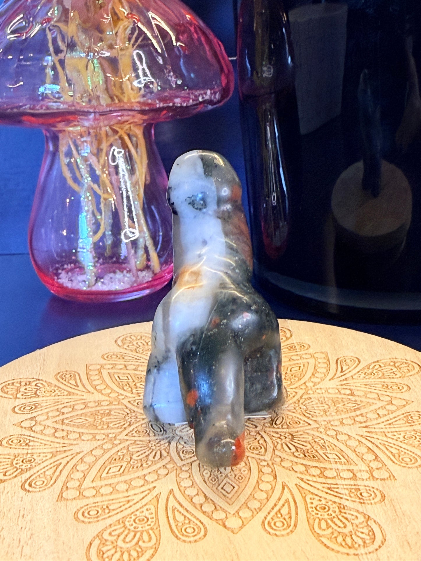 Multicolored bloodstone crystal sitting in front of a mushroom vase and black jar