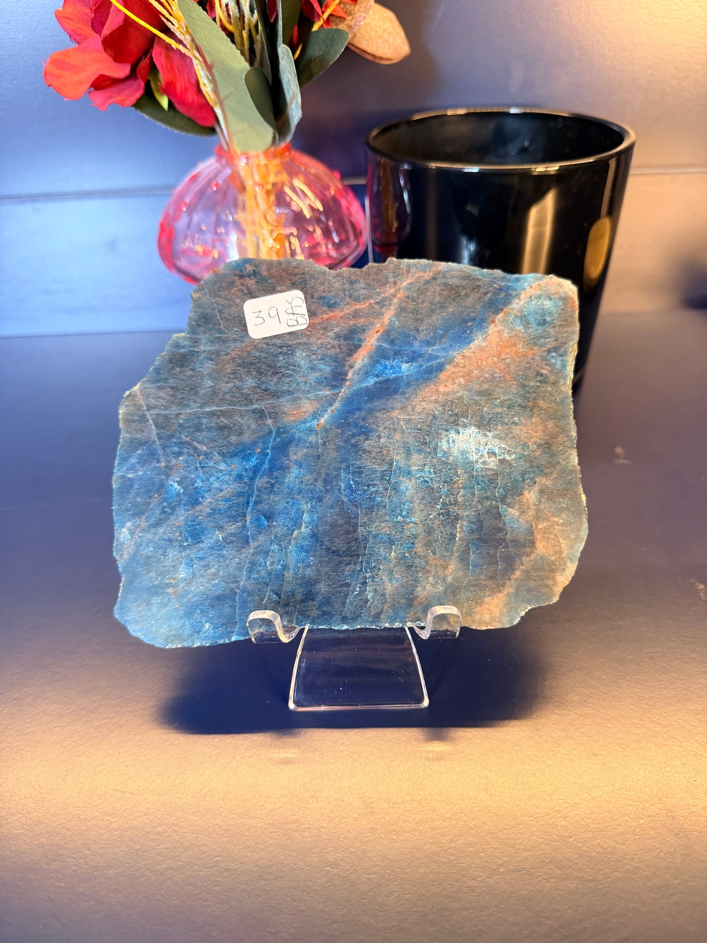 A large rough blue apatite slab sitting in front of a mushroom vase and black jar