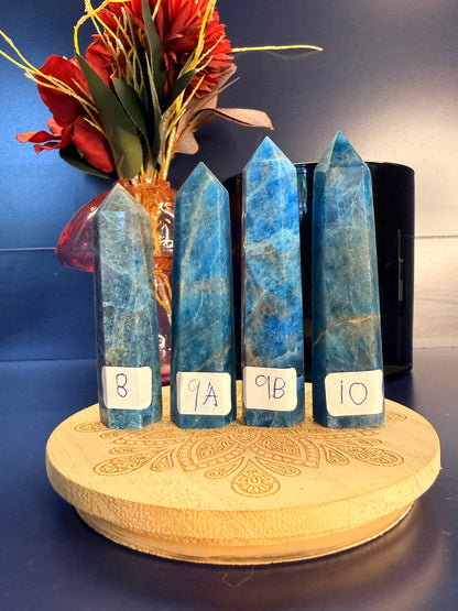 Four marbled blue apatite towers on a wooden coaster in front of a red flower and black vase