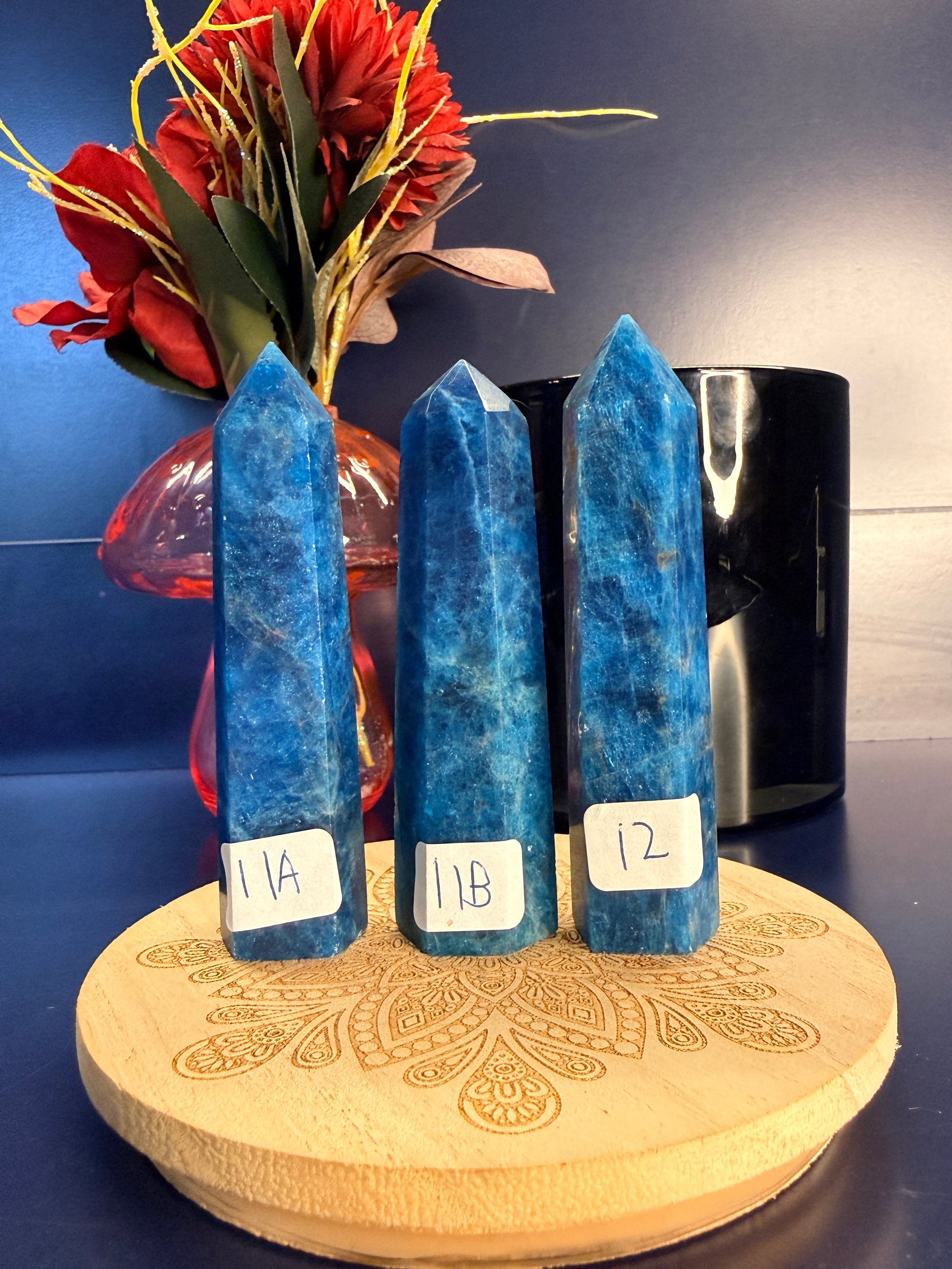 Three marbled blue apatite towers on a wooden coaster in front of a red flower and black vase