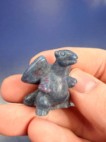 Hand holding a blue calcite crystal carving of a charizard-inspired creature against a blue background