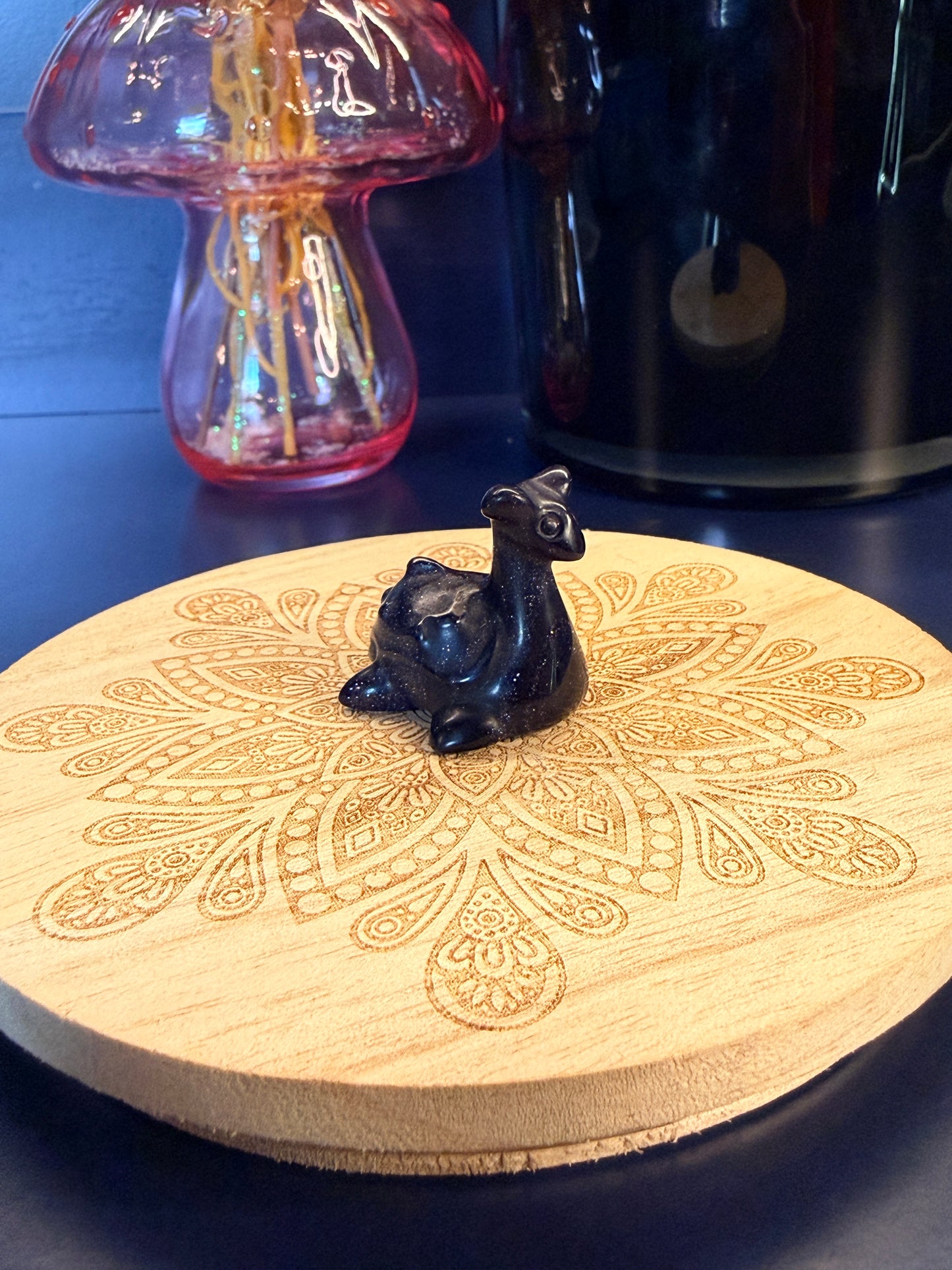 A blue goldstone lapras crystal sitting on a decorative wooden coaster in front of a glass mushroom and black jar