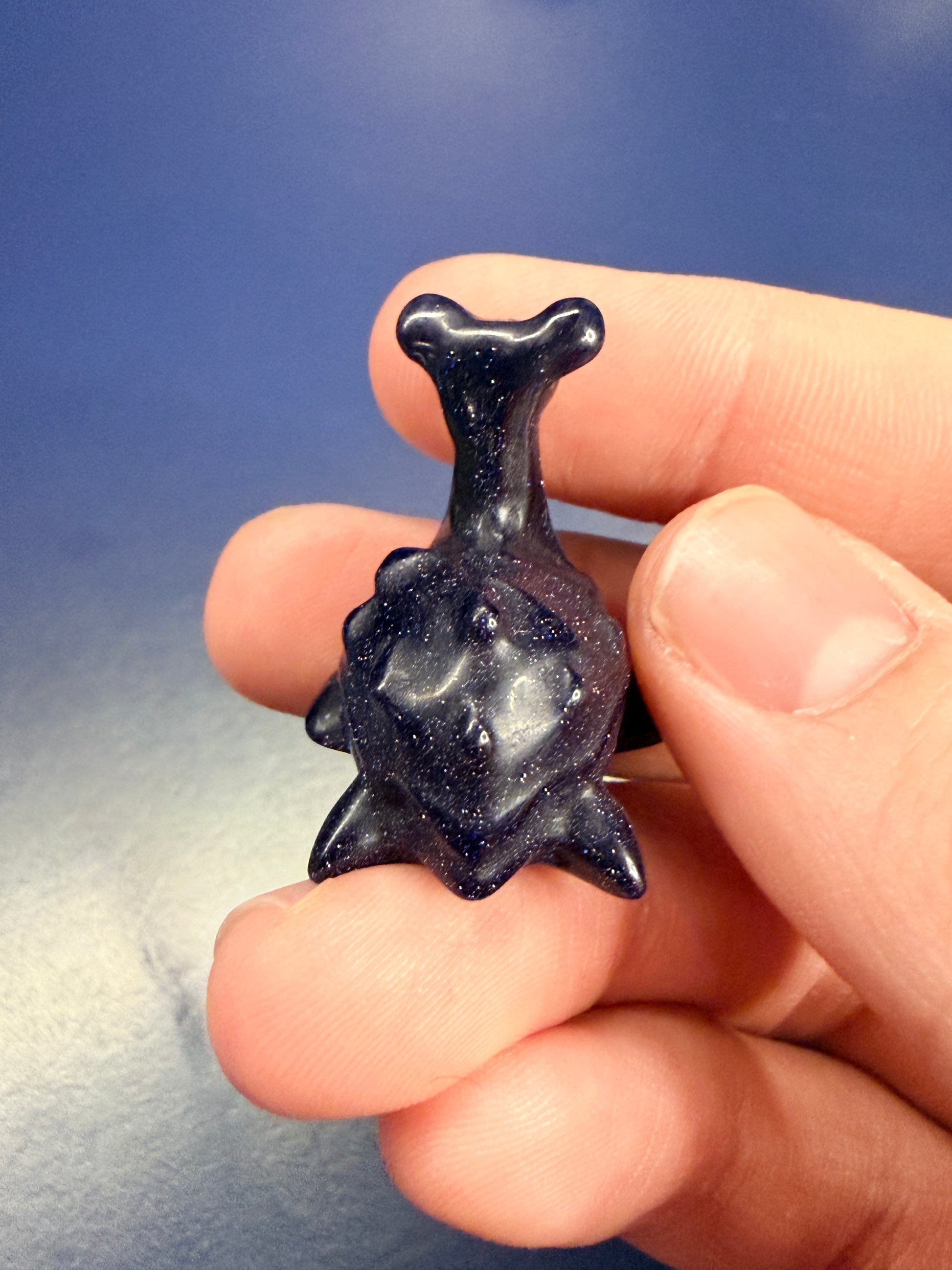 Hand holding a blue goldstone lapras crystal against a blue background