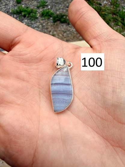 Hand holding an oblong blue lace agate sterling silver pendant in front of blurred nature background