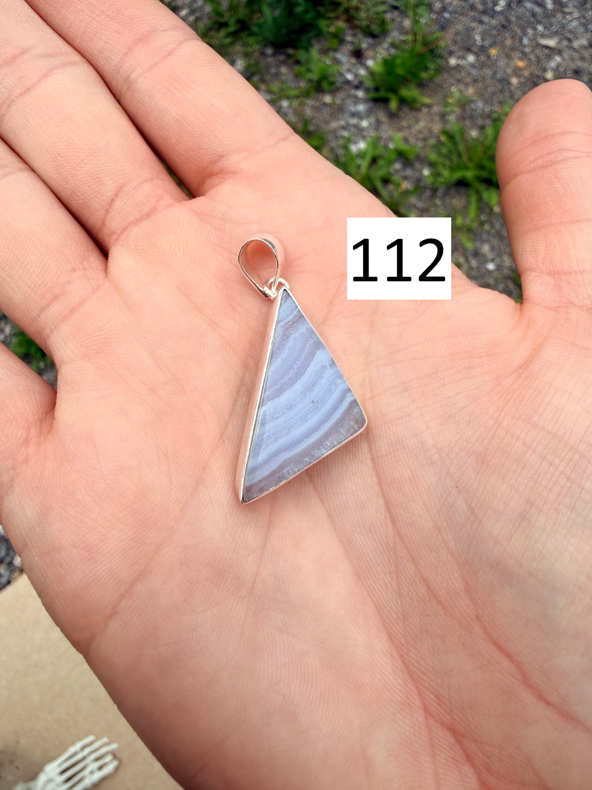 Hand holding a triangular-shaped blue lace agate sterling silver pendant in front of blurred nature background