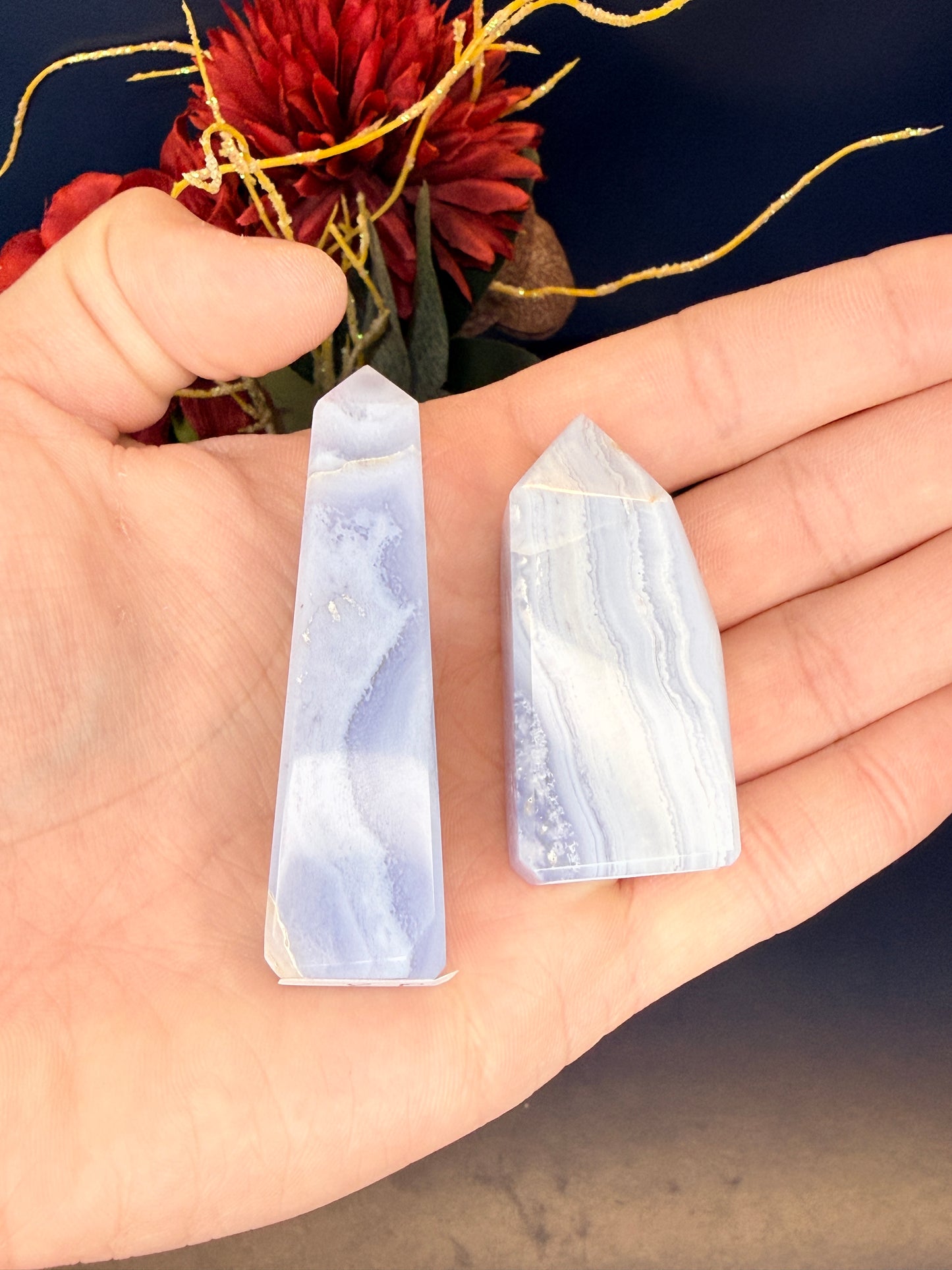 Hand holding two light blue patterned blue lace agate towers in front of a red flower
