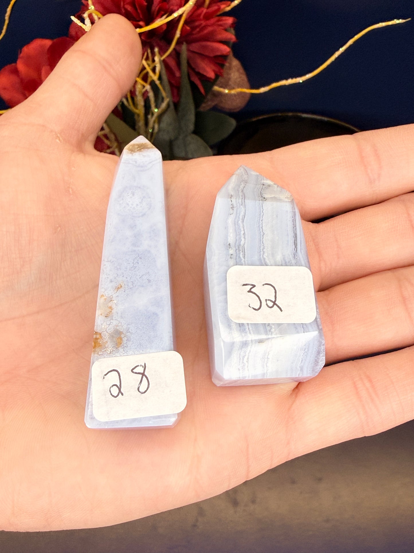 Hand holding two light blue patterned blue lace agate towers with labels in front of a red flower