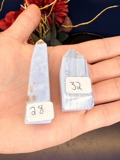 Hand holding two light blue patterned blue lace agate towers with labels in front of a red flower