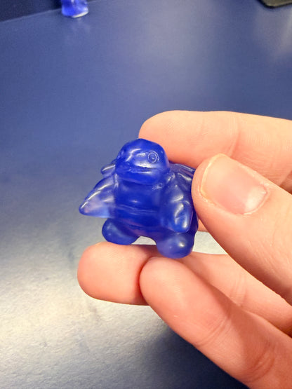 Hand holding a blue opalite blastoise crystal against a blue background