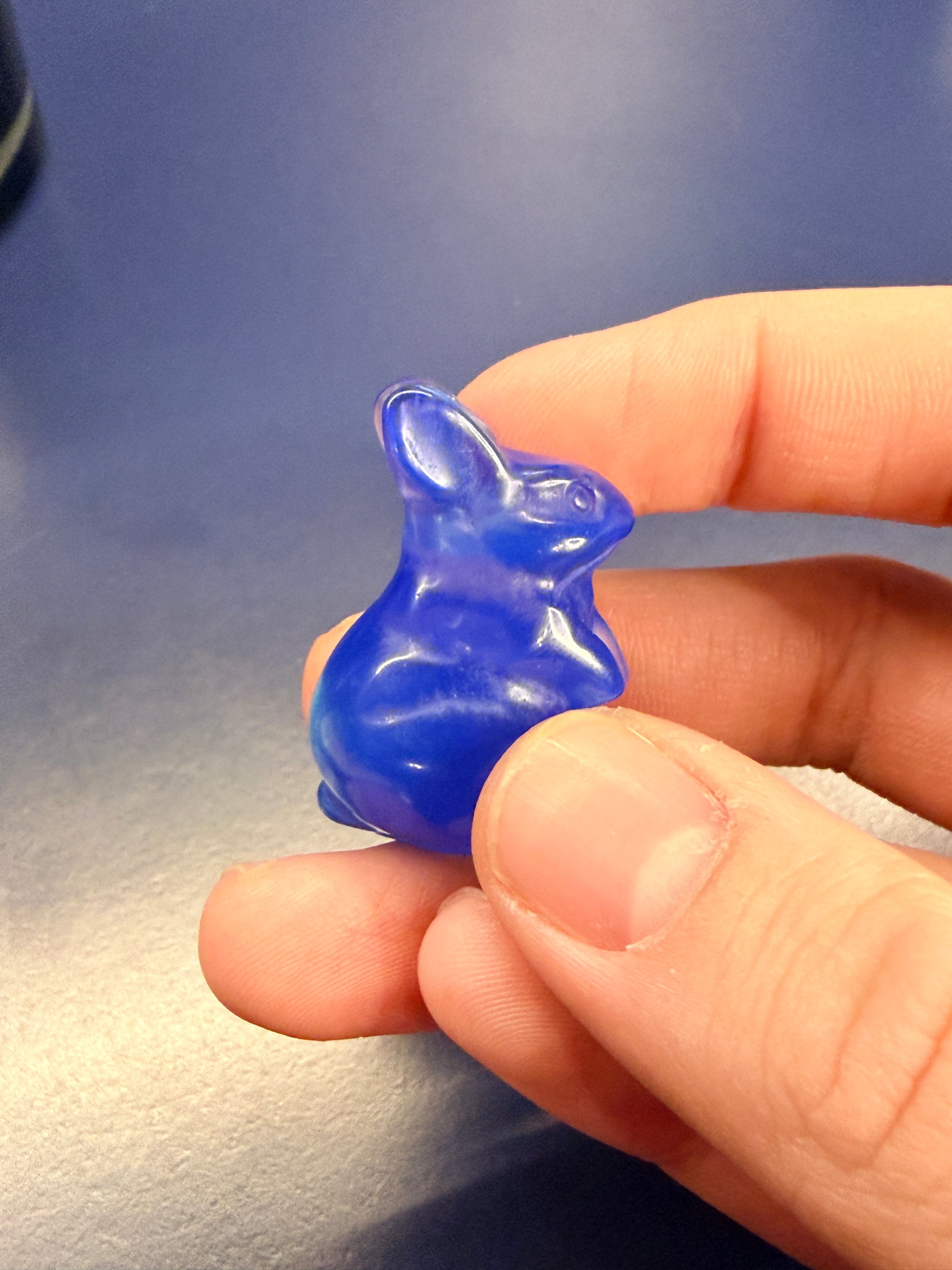 Hand holding a blue opalite bunny crystal against a blue background