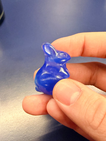 Hand holding a blue opalite bunny crystal against a blue background
