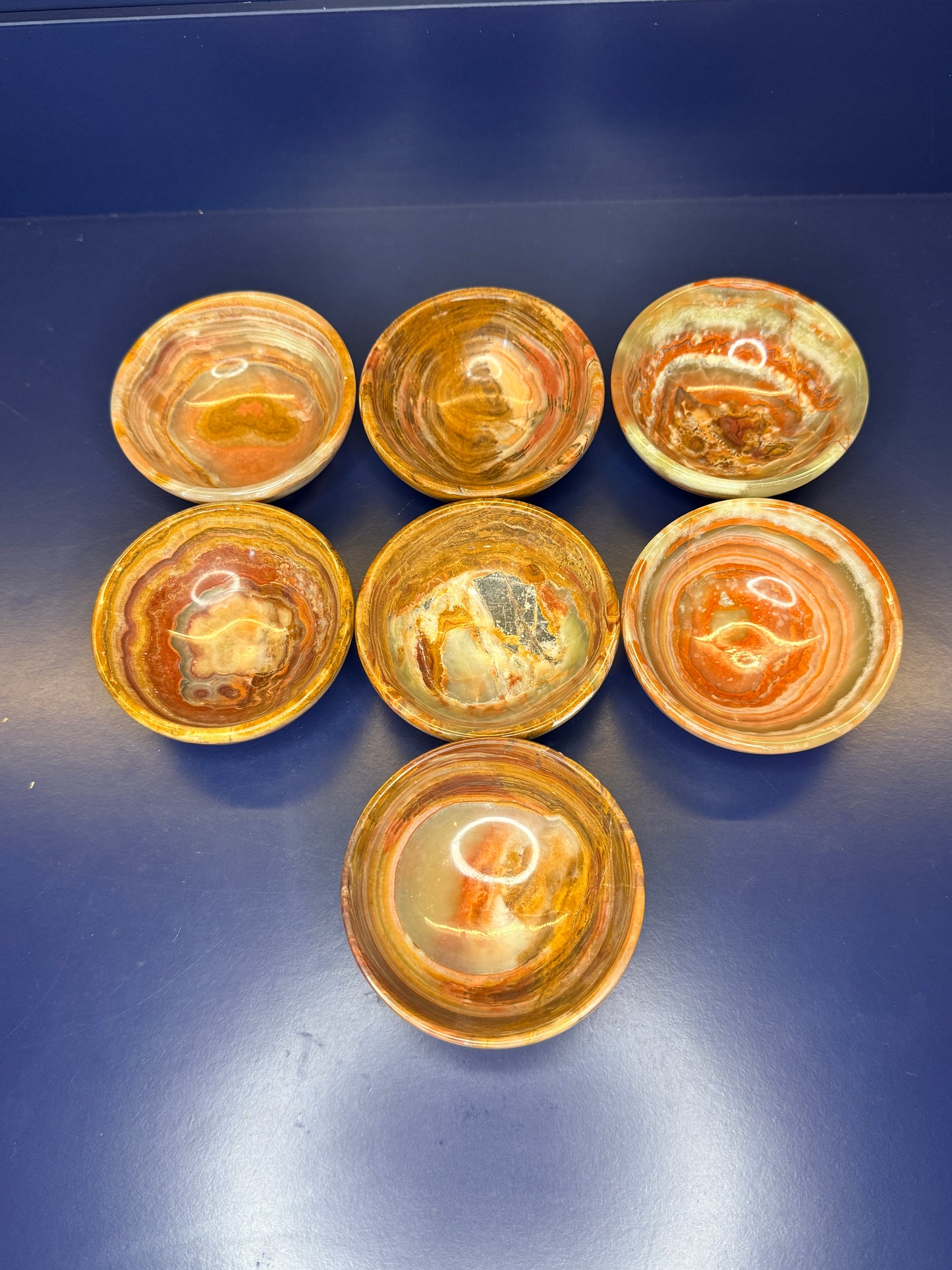 Seven green and brown green onyx bowls on a dark blue background