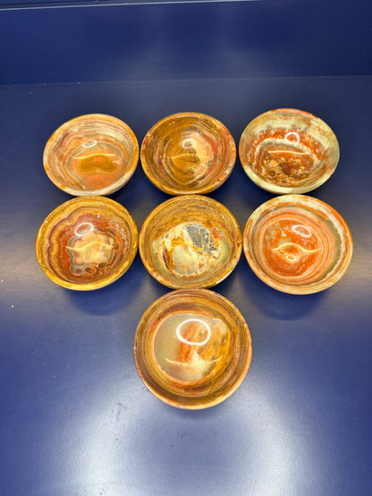 Seven green and brown green onyx bowls on a dark blue background