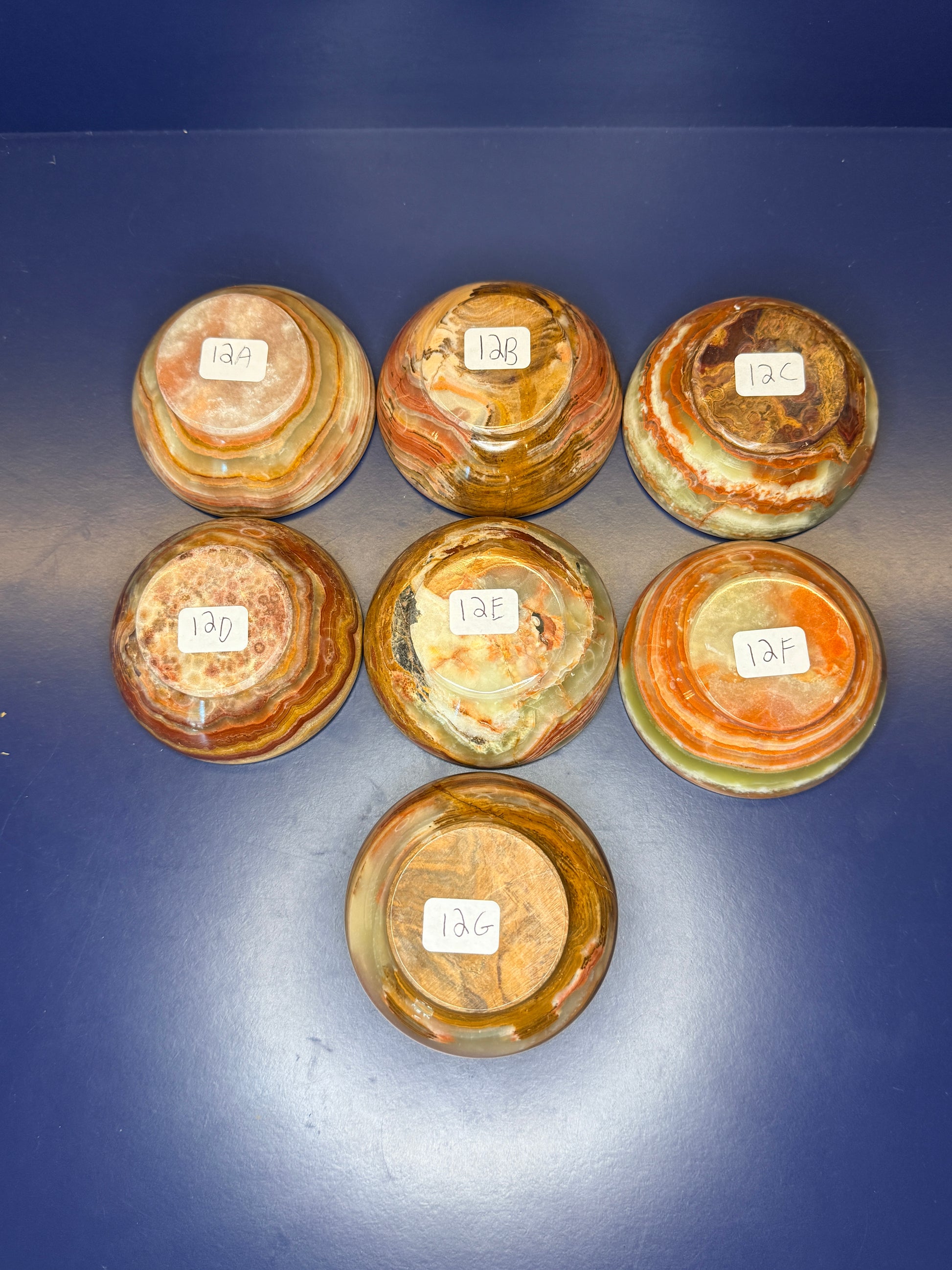Seven green and brown green onyx bowls with labels on a dark blue background