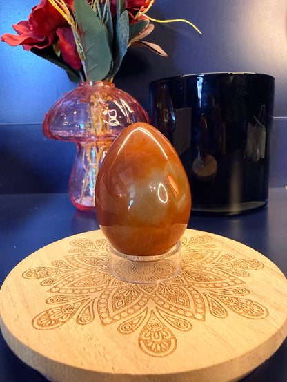 A red crystal egg sitting on a decorative wooden coaster in front of a glass mushroom and black jar