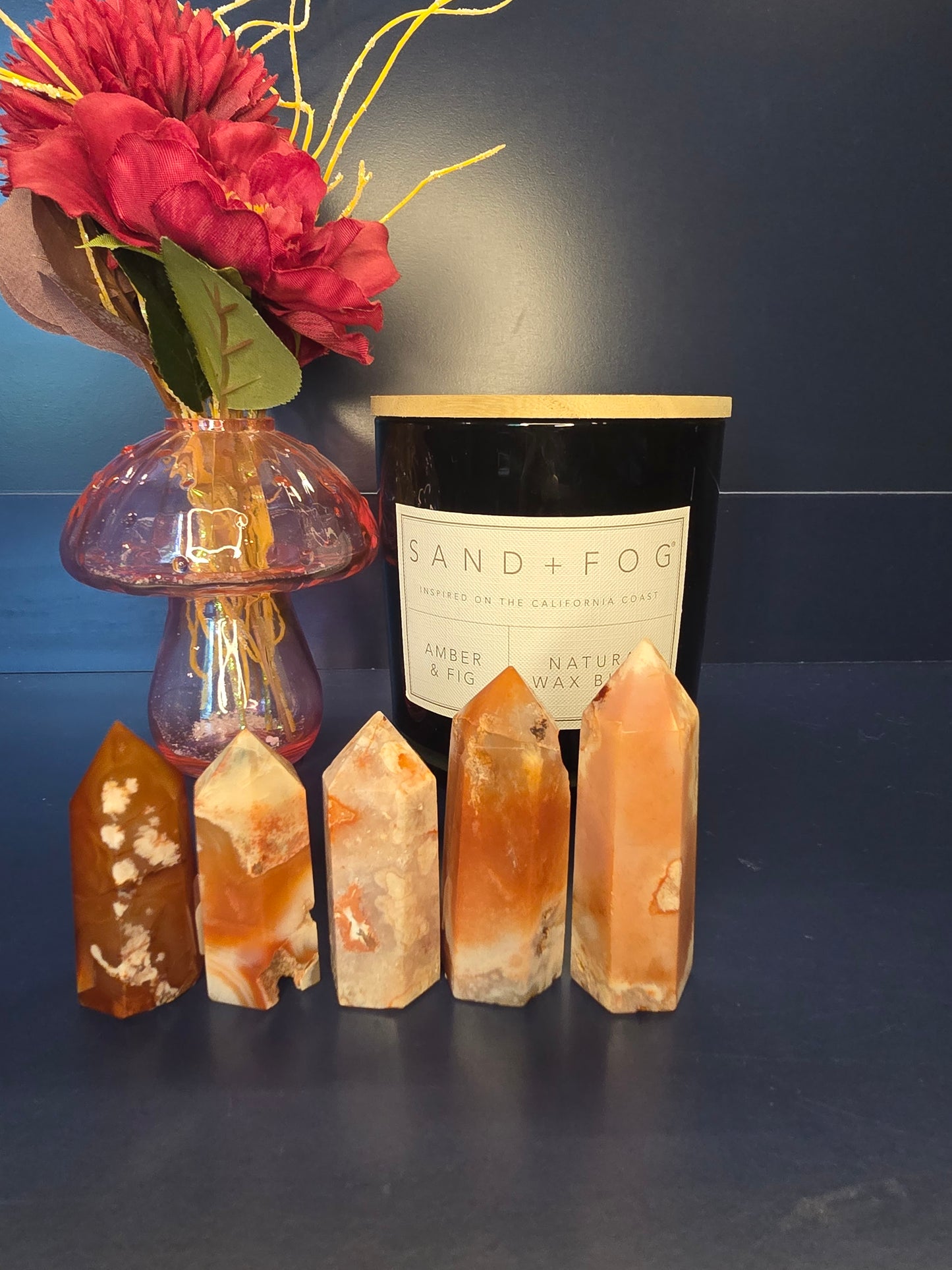 Five white, orange, and red crystal towers in front of a red flower in a vase and a black candle jar