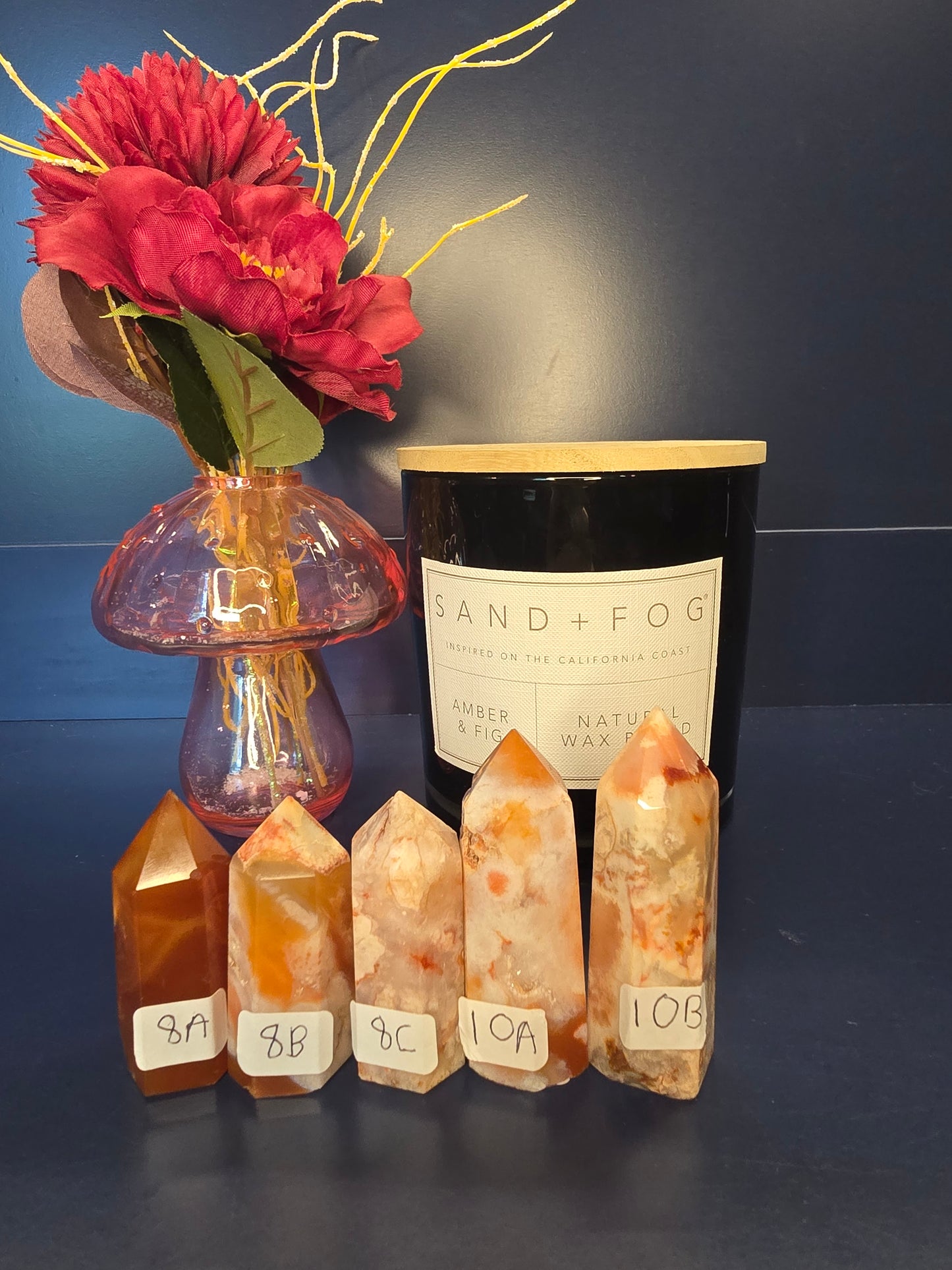 Five white, orange, and red crystal towers with numbered labels in front of a red flower in a vase and a black candle jar