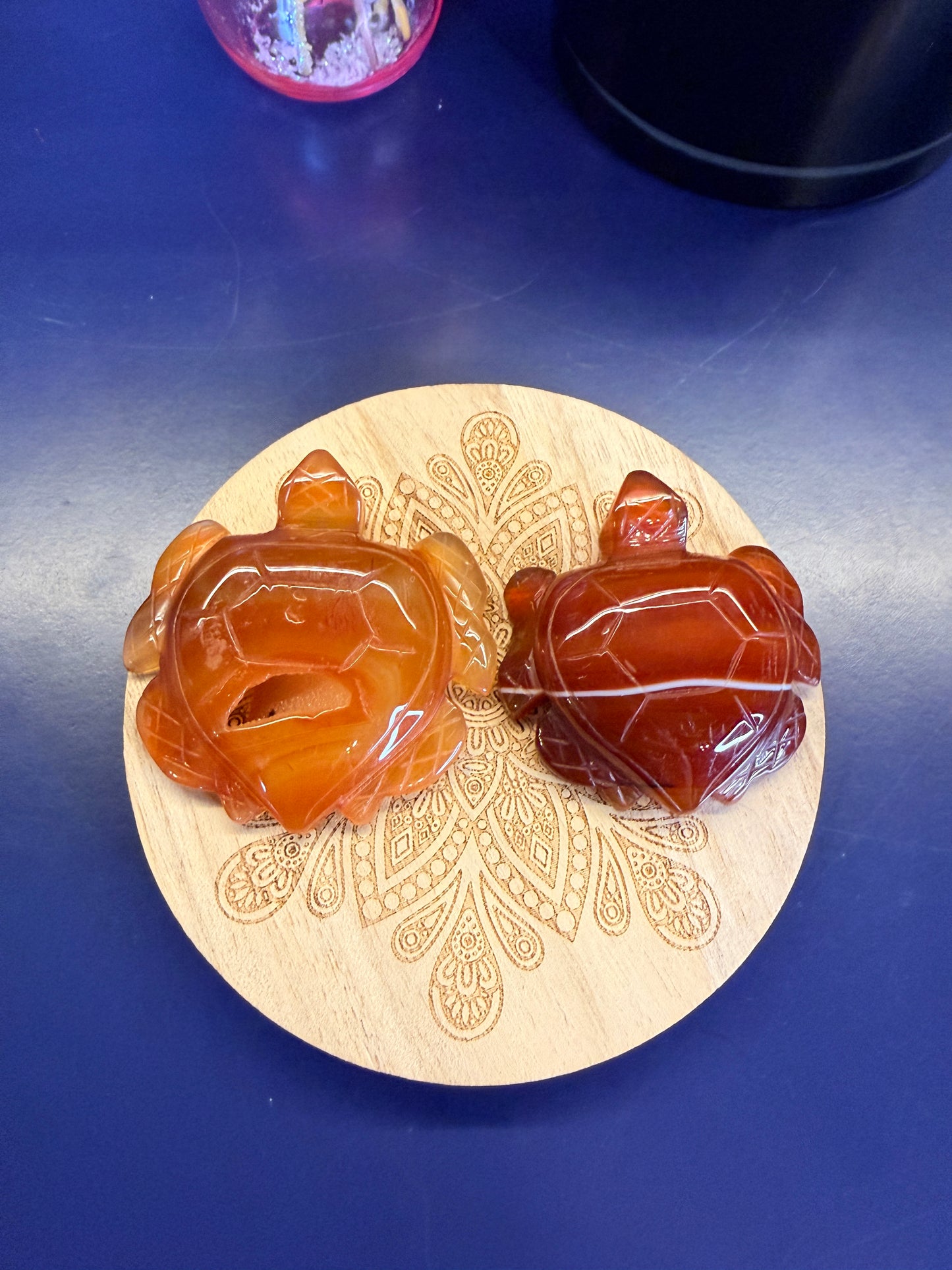 Two red carnelian turtles sitting on a decorative wooden coaster on a blue background