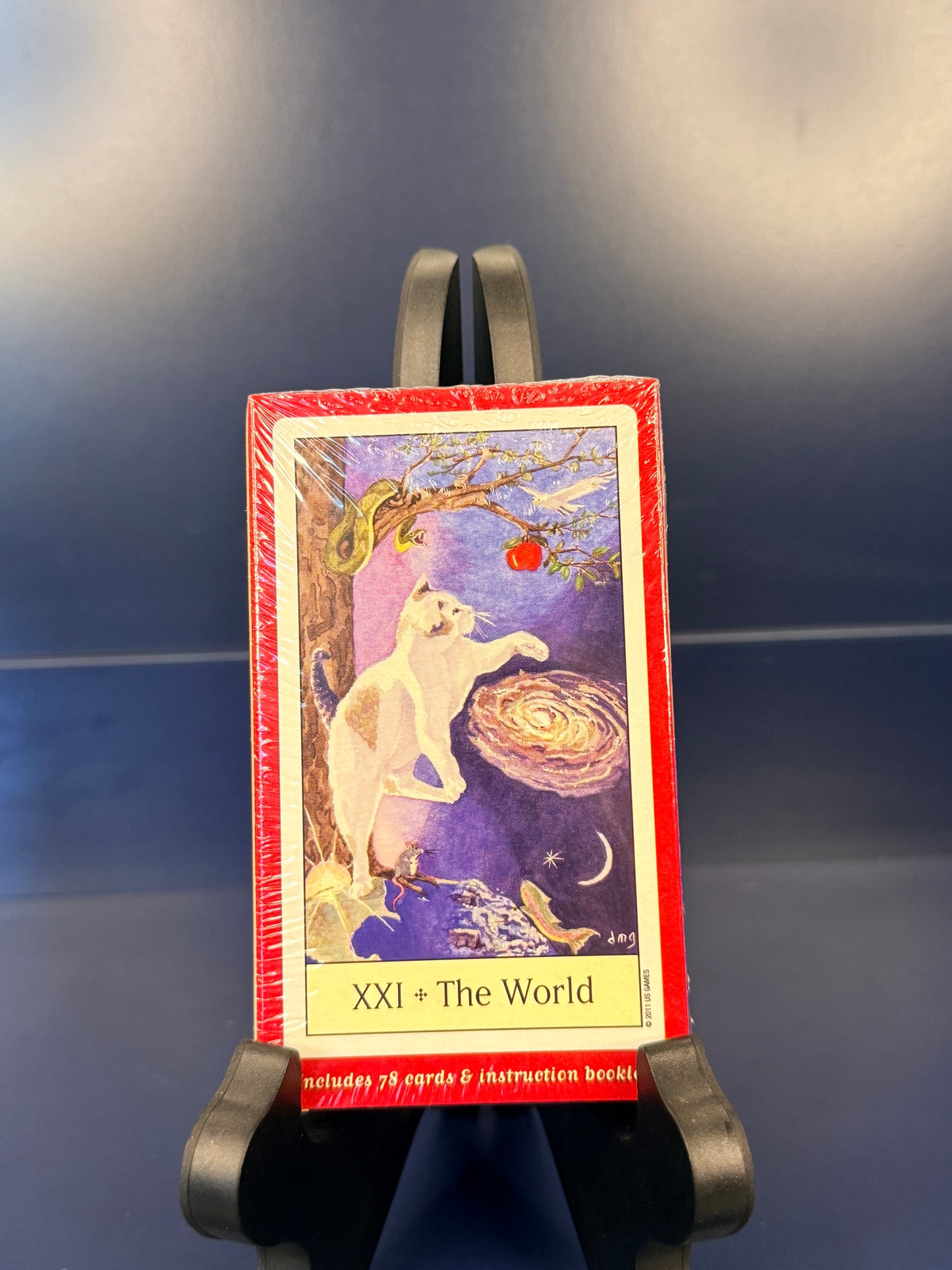 Back of Cat's Eye Tarot showing  "The World" on a black stand against a blue background