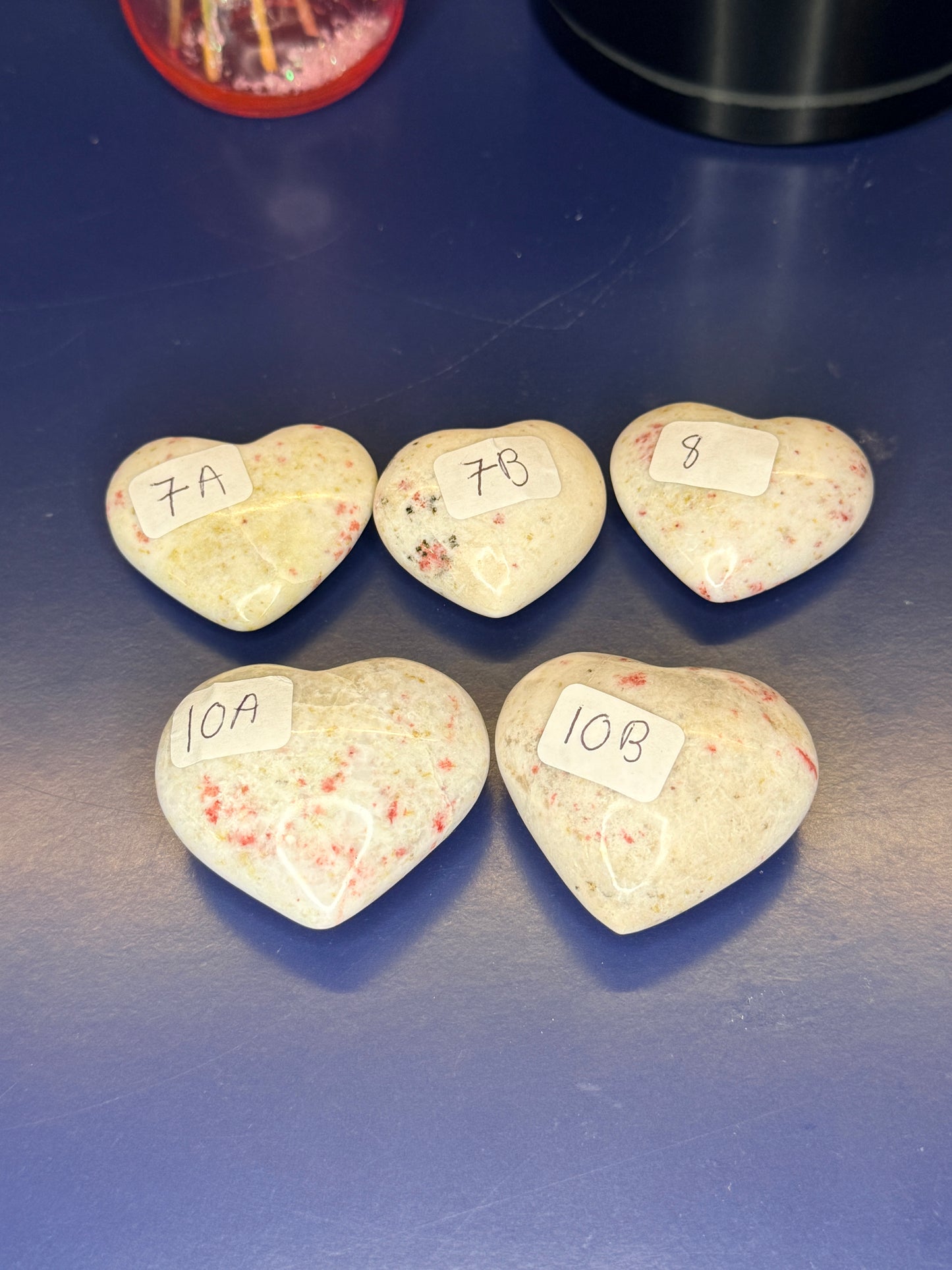 Five white and red speckled cinnabar hearts with numbered labels on a blue background
