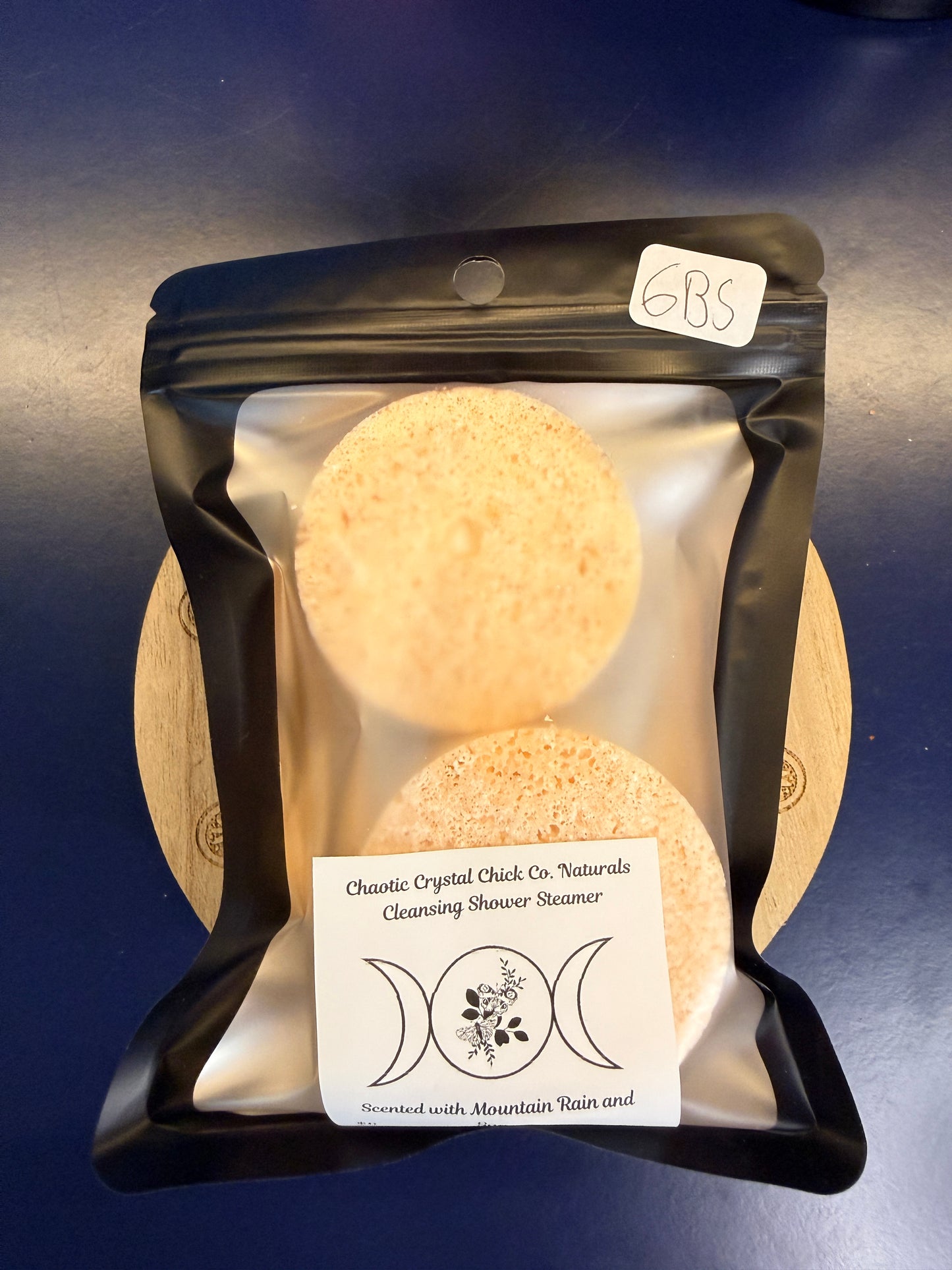 Packaged orange shower steamers on a decorative wooden coaster on a blue background