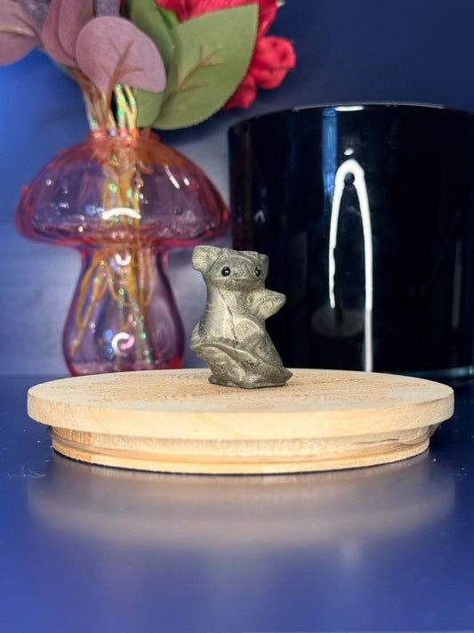 Golden pyrite baby dragon carving in front of a pink vase and black jar on a wooden coaster against a blue background