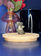 Golden pyrite baby dragon carving in front of a pink vase and black jar on a wooden coaster against a blue background