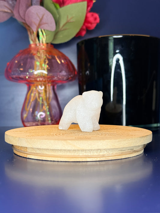 Clear quartz bear carving in front of a pink vase and black jar on a wooden coaster against a blue background