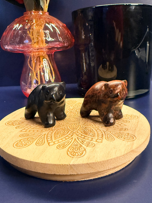 Two crystal bears sitting on a decorative wooden coaster in front of a glass mushroom and black jar