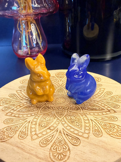 Two crystal bunnies sitting on a decorative wooden coaster in front of a glass mushroom and black jar